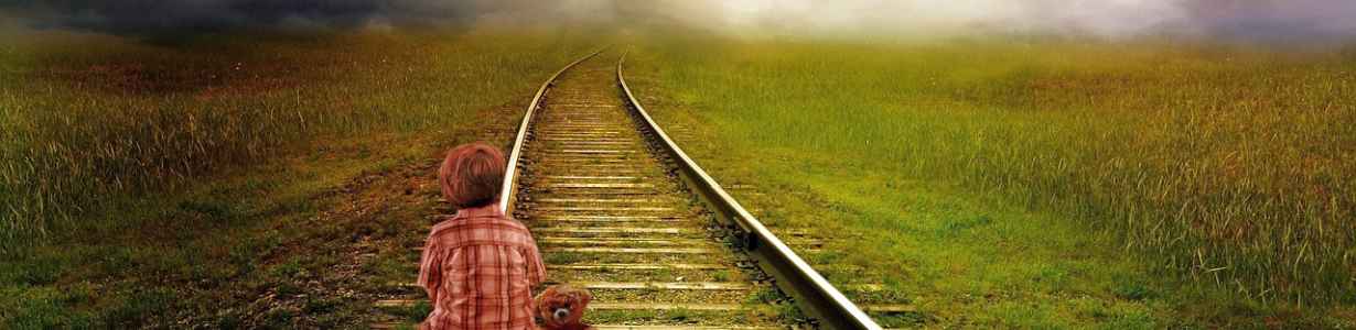 Young boy sitting on railroad tracks gazing on horizon